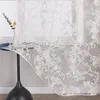 A close-up of a sheer curtain with an ornate pattern, draped over a small table with a vase and a single flower. Produktbild-Vorschau