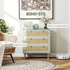 A boho-style dresser with rattan drawer fronts is shown in a living room setting, next to a wicker chair and a round rug. Produktbild-Vorschau