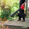 A person is using a leaf blower in an outdoor setting with trees and a railing. Produktbild-Vorschau