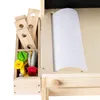 A close-up view of a wooden toy workbench with various tools and accessories stored in compartments, and a roll of white paper on the side. Náhled obrázku produktu