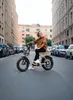 A woman is sitting on an electric bike on a city street. Produktbild-Vorschau