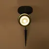 A solar-powered spotlight with a stake is shown against a light brown wall. Produktbild-Vorschau