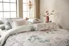 A beautifully made bed with floral bedding and decorative pillows, set against a window with natural light. Produktbild-Vorschau