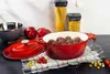 A red cast iron pot with meatballs inside, next to a lid, bell peppers, cherry tomatoes, and containers of pasta on a kitchen counter. Anteprima dell’immagine prodotto