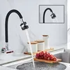 A kitchen faucet with a flexible black hose is shown mounted on a wall, with water flowing into a sink. There are also some kitchen containers and grapes in the foreground. Náhľad obrázku produktu