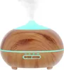 A light brown humidifier with a wood grain finish is shown against a white background, emitting a stream of mist and illuminated by a soft blue light. Náhled obrázku produktu