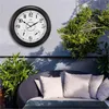 A large wall clock with thermometer and hygrometer mounted on an outdoor wall, next to a patio sofa with cushions. Produktbild-Vorschau