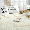 A cozy bedroom scene with a cream-colored blanket, pillows, and a bedside table. Podgląd zdjęcia produktu