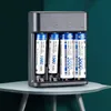 A battery charger with four AA/AAA rechargeable batteries inserted, placed on a light gray table against a dark green background. Podgląd zdjęcia produktu