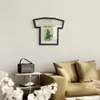 A living room scene with a t-shirt shaped photo frame on the wall, a couch with pillows, and a small table with a speaker. Náhled obrázku produktu
