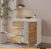 A white sideboard with wood-grain drawers and a door, placed in a room with a plant and a lamp. Produktbild-Vorschau