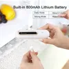 A hand holding a white air purifier with a charging cable nearby, with fruit in the background. Náhľad obrázku produktu