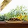 A wooden bowl filled with dried grasshoppers sits on a wooden surface, with a blurred background of greenery and yellow flowers. Produktbild-Vorschau