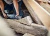 A person is using a reciprocating saw to cut a wooden beam in what appears to be an attic or construction site. Voir les images du produit