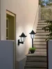 Two black outdoor lamps are mounted on a white wall next to a wooden staircase. Produktbild-Vorschau