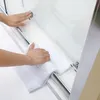 A person's hands cleaning a glass shower door with a white towel. Voir les images du produit