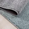 A close-up view of two rugs, one gray and one teal, layered on top of each other on a wooden floor. Podgląd zdjęcia produktu