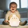 A baby sitting on a bed with a cute bunny-shaped night light. Produktbild-Vorschau