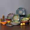 A collection of colorful, patterned ceramic dishes and bowls arranged on a wooden surface against a gray background. Produktbild-Vorschau