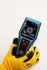 A hand wearing a yellow glove holds a blue and black digital wall scanner. Anteprima dell’immagine prodotto
