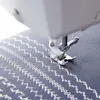 A close-up view of a sewing machine stitching decorative patterns on blue fabric. Produktbild-Vorschau