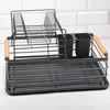 A gray metal dish rack with wooden handles sits on a light-colored countertop in front of a white tiled wall. Náhľad obrázku produktu
