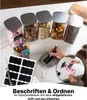 A collection of glass jars filled with various food items and candies, with a hand writing on a label. Anteprima dell’immagine prodotto
