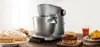 A kitchen mixer is shown with various food items, including cakes, a burger, and a salad, suggesting its versatility. Anteprima dell’immagine prodotto