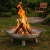 A metal fire pit with logs burning in a backyard setting, with a wooden chair in the background. Anteprima dell’immagine prodotto