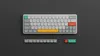 A top-down view of a compact mechanical keyboard and some loose keycaps, all set against a dark background. Produktbild-Vorschau