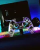 A transparent game controller with colorful LED lights is placed on a desk in front of a computer monitor. Produktbild-Vorschau