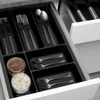 A close-up view of a black cutlery organizer drawer insert filled with various utensils and two small jars. Produktbild-Vorschau