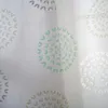 A close-up view of a white curtain with a repeating circular pattern of leaf-like shapes in turquoise, tan, and gray. Produktbild-Vorschau