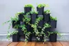 A vertical garden system with multiple black planters filled with green ivy plants, set against a gray wall and on a wooden deck. Produktbild-Vorschau