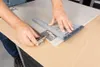 A person is using a specialized tool to measure and position a cabinet hinge on a door panel. Voir les images du produit
