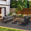 A modern outdoor patio with a grey sectional sofa, two wooden coffee tables, and lush greenery. Produktbild-Vorschau
