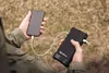 A person is holding a smartphone and a black power bank, with a cable connecting them. Anteprima dell’immagine prodotto