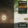A split image showing a night light plugged into a wall socket on the right, and a close-up of the night light in a dimly lit hallway on the left. Text overlays describe the product's features and benefits. Voir les images du produit