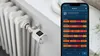 A smart radiator thermostat is attached to a radiator, with a smartphone displaying the control app in the foreground. Produktbild-Vorschau
