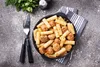 A bowl of pasta with meatballs and sauce, served with cutlery on a textured surface. Produktbild-Vorschau