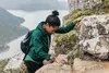 A woman is hiking up a rocky mountain, with a lake and mountains in the background. Voir les images du produit