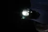 A close-up shot of a Nitecore HA11 headlamp attached to a dark blue baseball cap, illuminating the darkness. Podgląd zdjęcia produktu