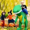 A man in an inflatable dinosaur costume is being ridden by two children dressed for Halloween, with pumpkins in the background. Náhled obrázku produktu