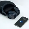 A pair of navy blue gaming headphones and a smartphone are placed on a white surface next to a black carrying case. Anteprima dell’immagine prodotto