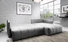 A modern, light gray sectional sofa with a chaise lounge is shown in a well-lit room with a large window and a brick wall. Produktbild-Vorschau