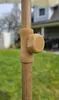 A close-up of a tan knob on a wooden pole, with a blurred outdoor background of grass and a house. Produktbild-Vorschau