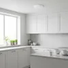 A clean, modern kitchen with white cabinets and countertops, featuring a large window and a ceiling light. Náhľad obrázku produktu
