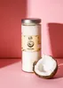 A jar of coconut oil and a halved coconut are placed on a pink surface with a pink background and shadows. Produktbild-Vorschau