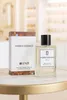 A perfume bottle and its box are displayed on a marble table with a blurred background of shelves. Produktbild-Vorschau