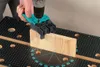A person is using a drill with a jig to drill a hole in a piece of wood on a workbench. Náhled obrázku produktu